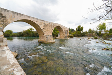 Fototapeta na wymiar Seljuk bridge in Aspendos. The Eurymedon Bridge. Aspendos Yolu Belkis Mevkii. Turkey. Crooked bridge. Bridge over the Kopruchay (Euremedon) River near Aspendos, in Pamphylia, in southern Anatolia