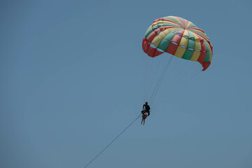 Two persons - man and child are parasailing. Colorful parachute, man holds from behind a child. Close up photo on clear blue sky