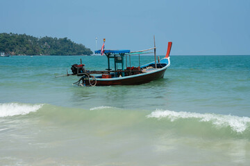 One Thai style wooden fishing boat anchored in sea close to coastline. Side view from the shore