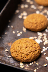 Craft and rustic four oatmeal cookies. Dark food aesthetics, black background with several oat flakes.