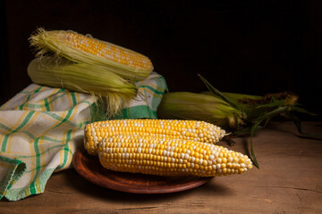 Clay plate with two cobs sweet corn on wooden background..