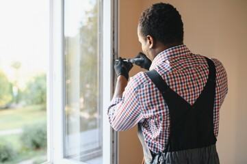 Close-up Of Young African Handyman In Uniform Installing Window