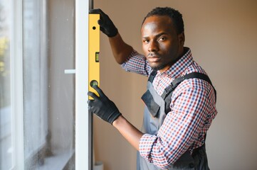 African american Workman in overalls installing or adjusting plastic windows in the living room at home