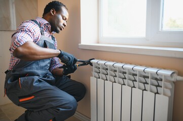 afro repairman in overalls using tools while installing or repairing heating radiator