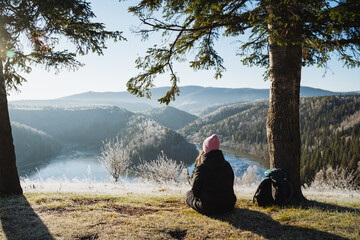 The girl is sitting on the ground and looking at the beautiful winter landscape, traveling in the mountains, time for meditation and yoga practice, relaxing in silence, peace.