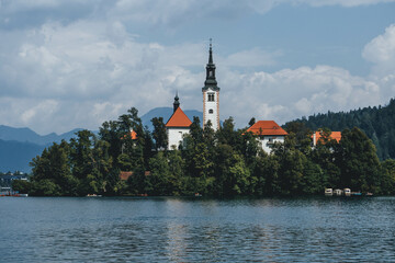 Fototapeta na wymiar tiny island with church tower and nature in the middle of gorgeous clear water blue lake 