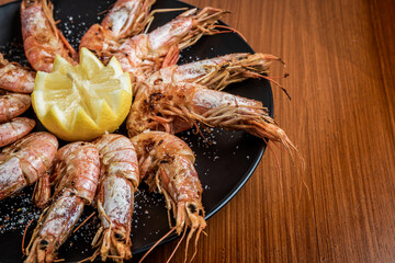 Horizontal close up photo of grilled prawns on black plate and wooden table. Gastronomy concept.