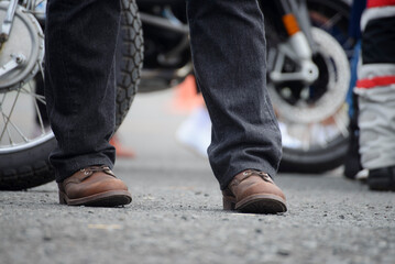 Legs of Lonely man wearing jeans and leather boots stand beside motorcycle. Travel Trip and...