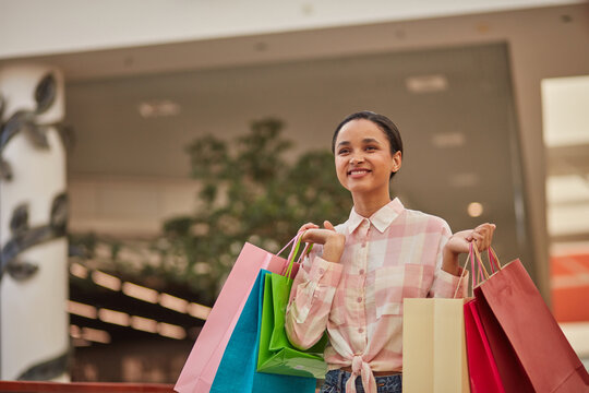 A woman carrying shopping bags in a store, smiling and enjoying a shopping trip.