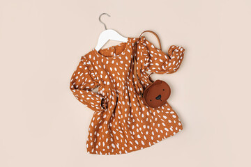 Stylish kids dress with cute handbag on a hanger on a beige background. Fashion kids outfit and accessories for summer or autumn.