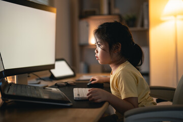 Asian baby girl wearing t-shirt concentrate to use laptop and study online on wood table desk in living room at home at night. Education learning online from home concept. - Powered by Adobe