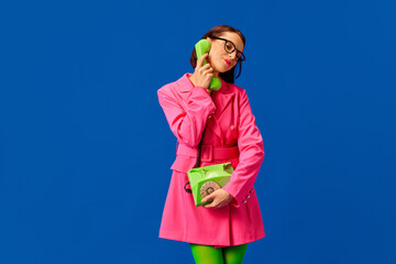 Young pretty woman, business lady dressed smart casual vivid outfit and style glasses talking on retro phone isolated blue background.