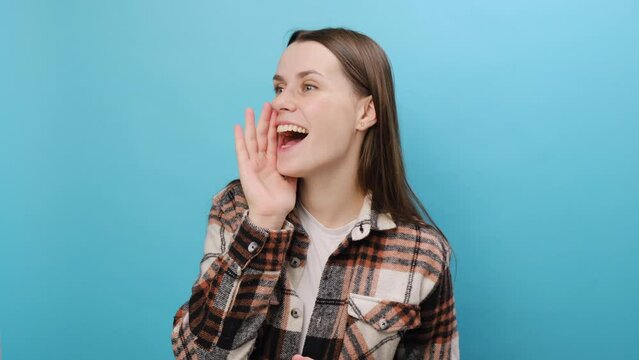 Portrait of excited happy fun young woman 25s wear casual shirt scream hot news about sales discount with hands near mouth hurry up, posing isolated over pastel blue color background wall in studio