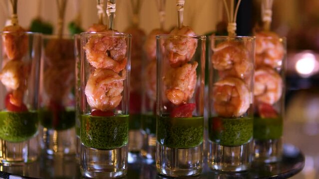 buffet snacks in long glass glasses caprice salad with pesto sauce shrimp skewered in portions. In a dark restaurant on glass trays portioned food