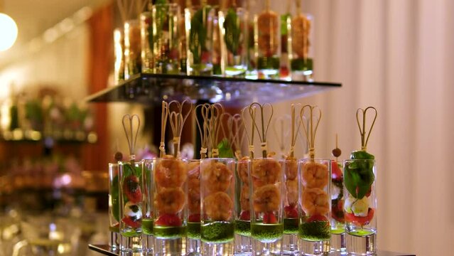 buffet snacks in long glass glasses caprice salad with pesto sauce shrimp skewered in portions. In a dark restaurant on glass trays portioned food