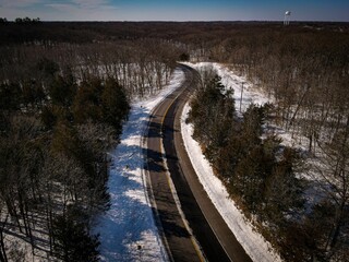 Aerial view of an asphalt road in a forest in winter surrounded by trees