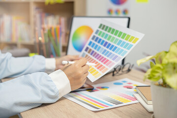 Designer at work on a table, selecting color shades for creative graphic design with laptop