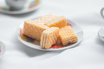 Galletas tipo gaufrette montadas en un plato acompañados con una tasa de té adornada con flores