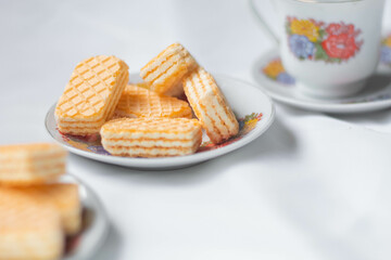 Galletas tipo gaufrette montadas en un plato acompañados con una tasa de té adornada con flores