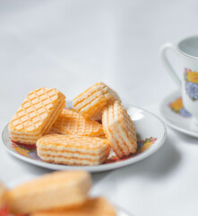 Galletas tipo gaufrette montadas en un plato acompañados con una tasa de té adornada con flores
