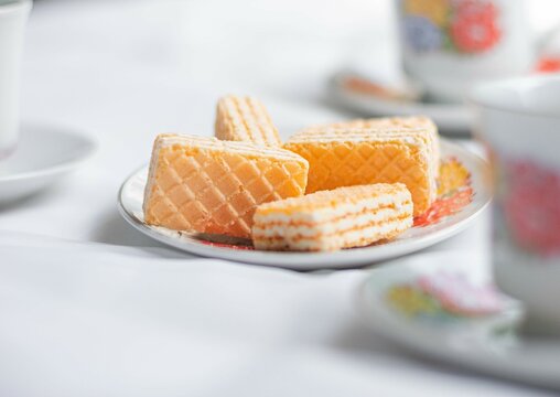 Galletas tipo gaufrette montadas en un plato acompa&ntilde;ados con una tasa de t&eacute; adornada con flores