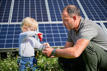 Dad showing to his little son how to use screwdriver in background of solar panels. Father teaching...