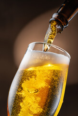 Jet of beer out of the bottle is poured into a beer glass, causing a lot of bubbles and foam.