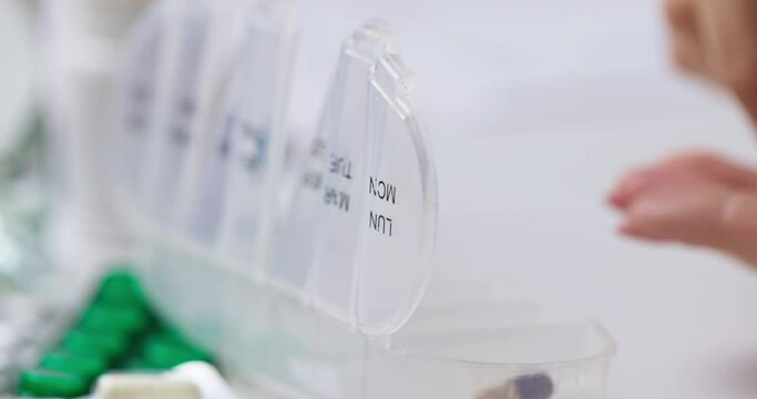 Woman hand putting pills into open pill organizer or plastic pillbox