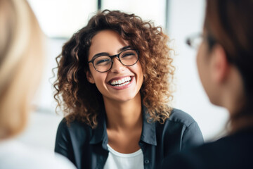 Picture of smiling woman wearing glasses engaged in conversation with another woman. This image can be used to depict friendship, communication, teamwork, or professional networking