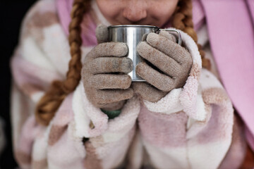 Close-up of female child in grey woolen gloves holding metallic mug with hot tea while sitting in...