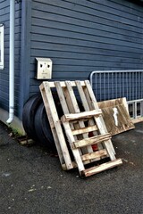 Vertical shot of a few car tires and wooden pallets next to a blue shed