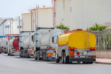 Parking row jam of trucks with fuel tanks in front of a warehouse and storage of huge tanks of raw...