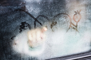 Part of steamy car window and child finger drawing heart on its surface while sitting inside...