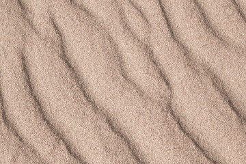 Fototapeta na wymiar Sandy wavy background. Coarse sand with a dune pattern, top view.