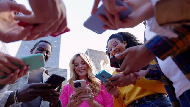 Happy group of young people using mobile phones outdoors. Teenage friends having fun together watching social media content on smart cell phone app, connected online. Technology lifestyle concept.