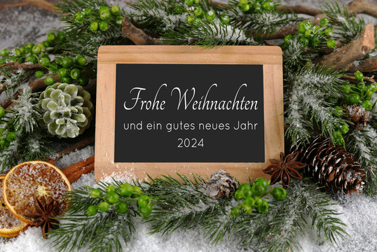 Weihnachtsgrüße auf einem Rahmen mit Tannengrün im Schnee. Frohe Weihnachten und eine glückliches neues Jahr  2024.