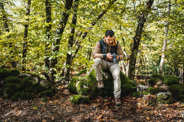 young and beautiful photographer resting on a stone in the forest after walking and photographing the wonders of the environment, while looking at the photographs in the camera