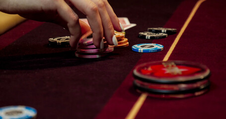 Close-up of hands playing poker with chips on red table.