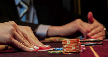 Close-up of hands playing poker with chips on red table.