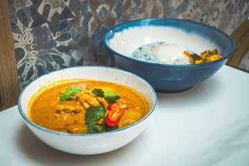 a bowl of curry chicken with potatoes and butterfly pea rice and pickled achar and fried egg