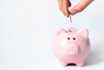 A woman's hand puts a coin into a piggy bank close-up on a white background. Business, investment,...