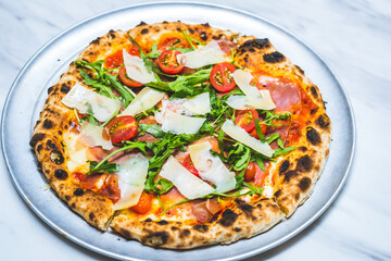 Neapolitan style pizza with cheese, patma ham, arugula, tomato sauce and cherry tomatoes