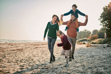 Happy family dressed in warm clothes walking on the beach