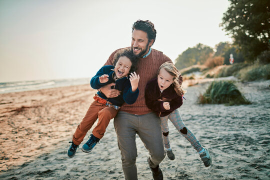 Father holding children on cold beach during sunset