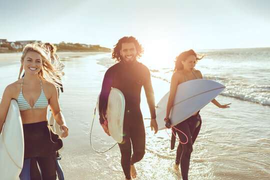 Young diverse surfers walking on shoreline ready to hit the waves together