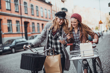 Two young Caucasian women friends shopping in town with bicycles
