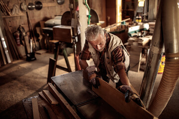 Senior male carpenter measuring wood on workbench in workshop