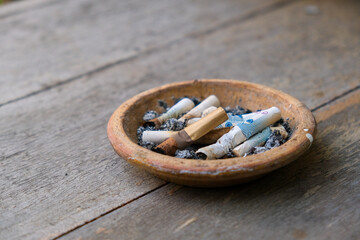 The part of cigarette butts are left in the ashtray put on the wooden table after it were being...