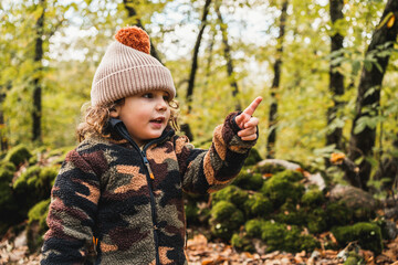 portrait of pretty fashionable little boy with hat in a forest pointing finger forward