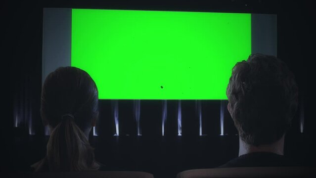 Green Screen Cinema Couple Watching Movie Theater Zoom In. Couple inside a movie theater watching a green screen projection with an old film texture, zoom in.